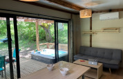 Interior view of a modern cottage with sofa, dining table, and outdoor hot tub at Campsite Le Luberon, France.