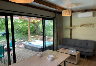 Vista interna di un cottage moderno con divano, tavolo da pranzo e vasca idromassaggio esterna a Camping Le Luberon, Francia.