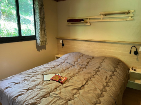 Camera moderna al Cottage «Pantaïa» del campeggio Le Luberon in Francia, con letto, finestra e libri sul letto.