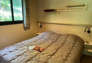 Camera moderna al Cottage «Pantaïa» del campeggio Le Luberon in Francia, con letto, finestra e libri sul letto.