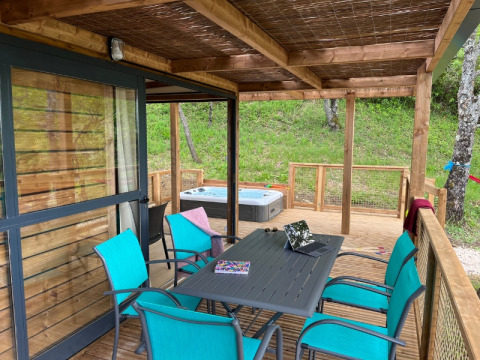 Veranda coperta al Cottage «Séouvo» con sedie turchesi, tavolo, portatile e vasca idromassaggio sul prato.