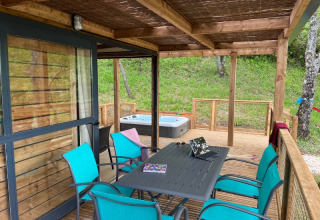 Veranda coperta al Cottage «Séouvo» con sedie turchesi, tavolo, portatile e vasca idromassaggio sul prato.