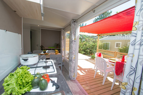 Cucina luminosa e terrazza coperta con tavolo nel Cottage Romarin al campeggio Le Luberon, Francia.