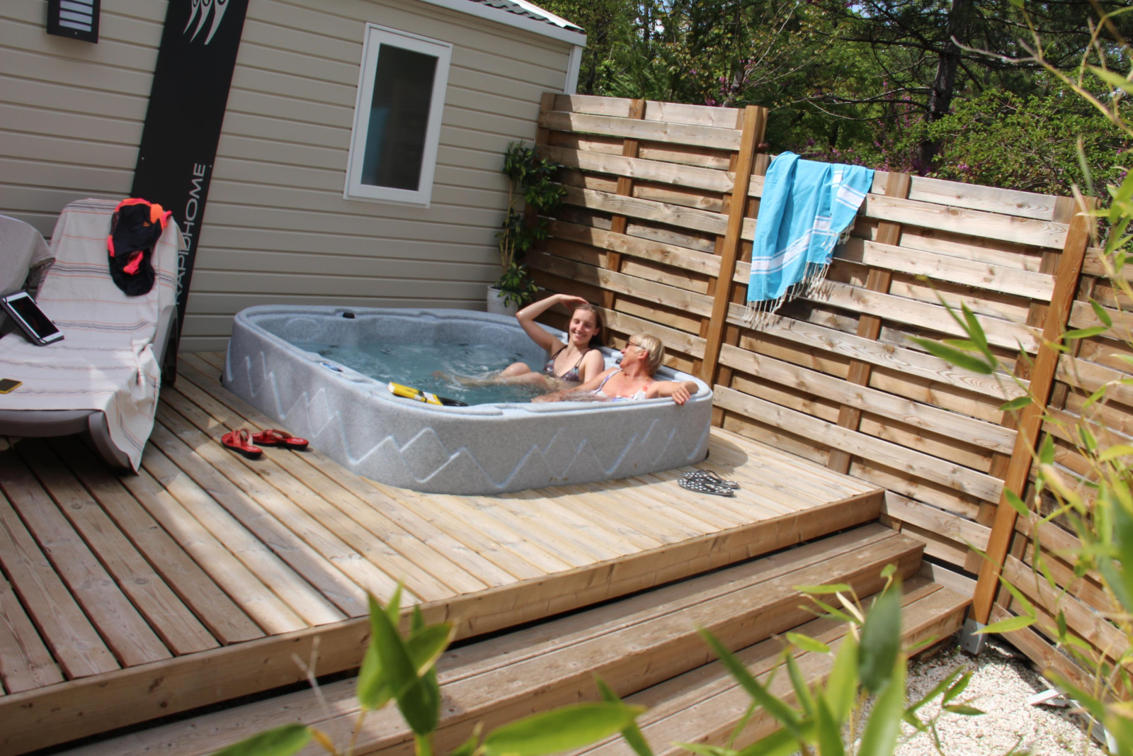 Twee mensen ontspannen in een bubbelbad op een houten terras bij Cottage Romarin, Camping Le Luberon, Frankrijk.