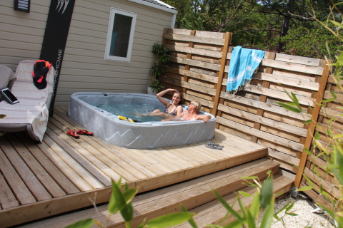 Due persone si rilassano in una vasca idromassaggio su una terrazza di legno al Cottage Romarin, Camping Le Luberon, Francia.