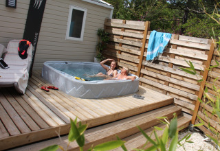 Due persone si rilassano in una vasca idromassaggio su una terrazza di legno al Cottage Romarin, Camping Le Luberon, Francia.