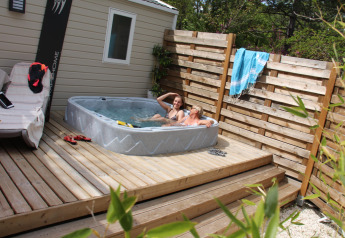 Due persone si rilassano in una vasca idromassaggio su una terrazza di legno al Cottage Romarin, Camping Le Luberon, Francia.