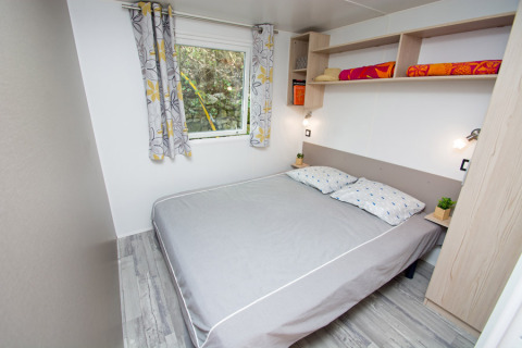 Camera da letto con letto matrimoniale, tende colorate, mensole e arredo moderno al Cottage Romarin, Camping Le Luberon.