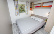 Camera da letto con letto matrimoniale, tende colorate, mensole e arredo moderno al Cottage Romarin, Camping Le Luberon.