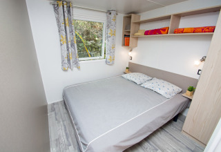Camera da letto con letto matrimoniale, tende colorate, mensole e arredo moderno al Cottage Romarin, Camping Le Luberon.