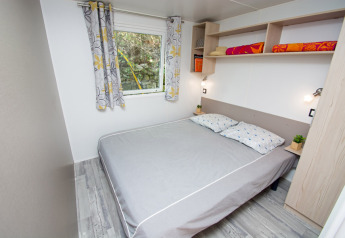 Camera da letto con letto matrimoniale, tende colorate, mensole e arredo moderno al Cottage Romarin, Camping Le Luberon.