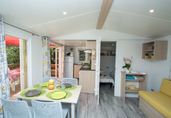 Interno del Cottage Romarin al campeggio Le Luberon in Francia con tavolo da pranzo e arredamento luminoso.