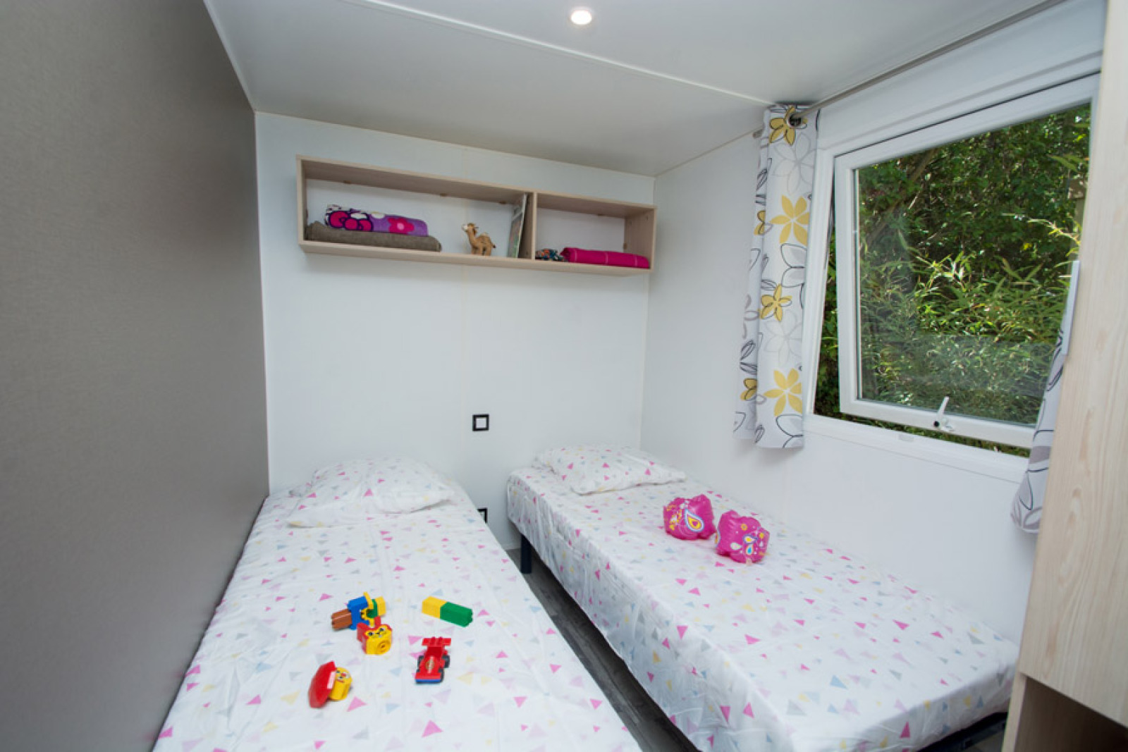 Lichte kinderkamer in Cottage Romarin op Camping Le Luberon in Frankrijk, met twee bedden en speelgoed.