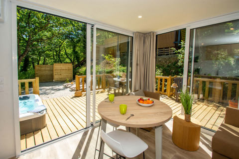 Interno di cottage luminoso con tavolo rotondo, terrazza in legno, idromassaggio e natura al Camping Le Luberon.
