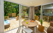 Bright cottage interior with round table, fruit bowl, large windows to deck, hot tub, and trees at Le Luberon.