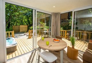 Interno di cottage luminoso con tavolo rotondo, terrazza in legno, idromassaggio e natura al Camping Le Luberon.