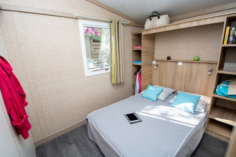 Camera da letto nel Cottage Lavande al Campeggio Le Luberon con letto matrimoniale, mensole e tablet.
