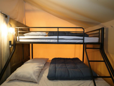 Etagenbett mit weißen und blauen Bettdecken in einem Premium-Safari-Zelt im Domaine des Chênes Blancs, Frankreich.