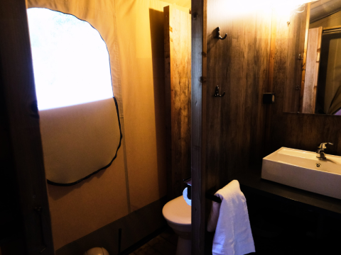 Badezimmer im PREMIUM Lodge Safarizelt im Domaine des Chênes Blancs, Frankreich, mit Waschbecken und Spiegel.