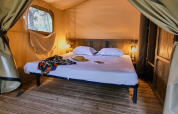 Interieur van een Lodge «COSY» safaritent bij Domaine des Chênes Blancs, Frankrijk, met houten vloer en bed.