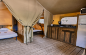 Interieur van de Lodge «COSY» safaritent op Domaine des Chênes Blancs in Frankrijk, met slaap- en keukenruimte.
