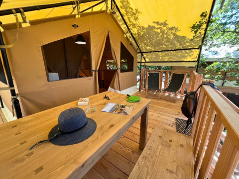 Wooden terrace at safari tent 'Bungalowtent', Domaine des Chênes Blancs, France, with table and chairs.