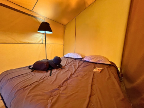 Gemütlicher Schlafbereich im Bungalowzelt Domaine des Chênes Blancs in Frankreich mit Lampe und Bett.