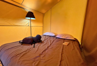 Gemütlicher Schlafbereich im Bungalowzelt Domaine des Chênes Blancs in Frankreich mit Lampe und Bett.