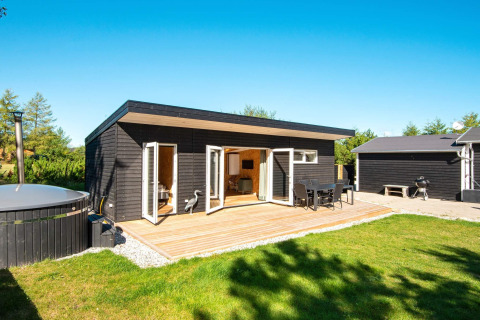 Moderne feriebolig med sort træfacade, stor træterrasse og udendørs spabad i Glesborg, Danmark.