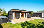 Moderne feriebolig med sort træfacade, stor træterrasse og udendørs spabad i Glesborg, Danmark.