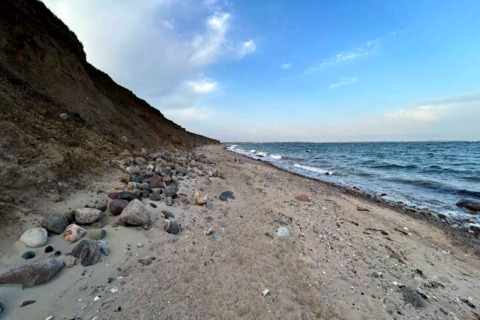 Littoral à Haderslev avec une plage de sable et de rochers, falaise à gauche, mer et ciel bleu à droite.