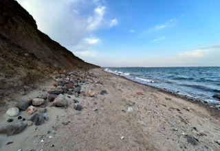 Küstenlinie bei Haderslev mit Steinen am Sandstrand, Klippe links, Meer und blauer Himmel rechts.