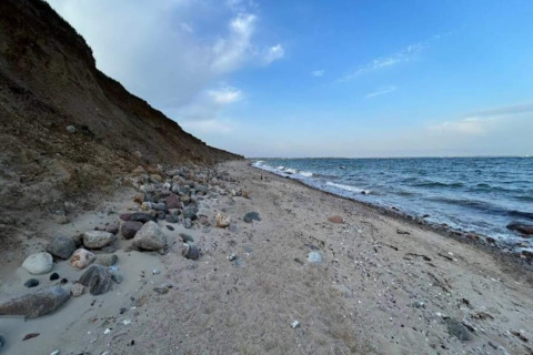 Littoral à Haderslev avec une plage de sable et de rochers, falaise à gauche, mer et ciel bleu à droite.