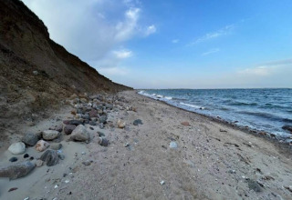 Littoral à Haderslev avec une plage de sable et de rochers, falaise à gauche, mer et ciel bleu à droite.