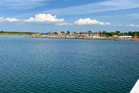 Vista sull’acqua verso un porto turistico e case a Haderslev, Danimarca, con cielo azzurro e nuvole.