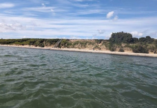 Vue sur l’eau et la plage près du 'gîte pour 4 personnes à Haderslev', Danemark, par une journée ensoleillée.