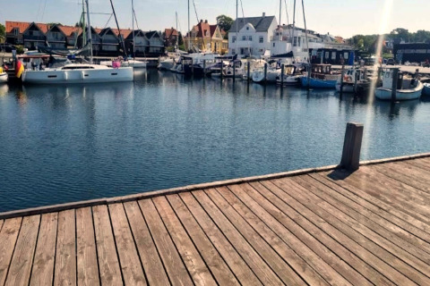 Billede af en lystbådehavn med både og huse i baggrunden taget fra træmole ved 4 personers feriehus i Haderslev.