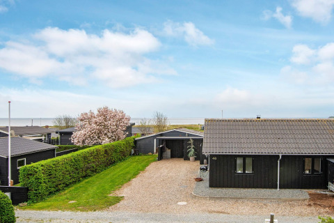 Maison de vacances noire avec allée gravillonnée et vue sur la mer à Haderslev, Danemark, sous ciel bleu.