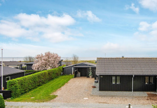 Maison de vacances noire avec allée gravillonnée et vue sur la mer à Haderslev, Danemark, sous ciel bleu.