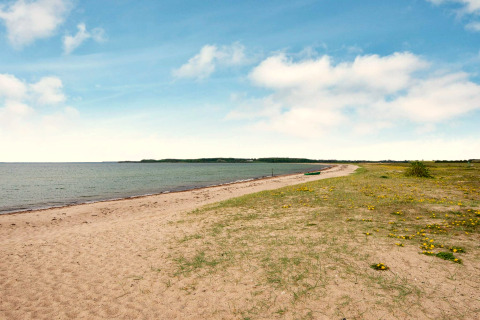 Strandbillede fra Haderslev, Danmark med sand, grønt græs og en båd under blå himmel.