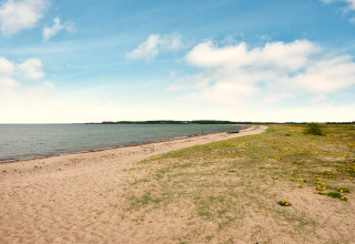 Strandbillede fra Haderslev, Danmark med sand, grønt græs og en båd under blå himmel.