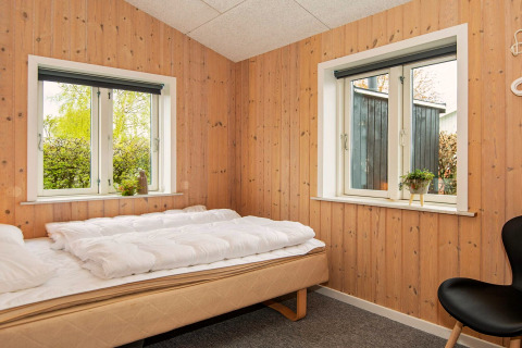 Camera da letto con pareti in legno, due finestre, letto singolo e arredo semplice a Haderslev, Danimarca.