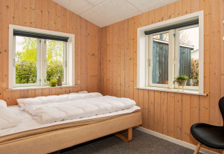 Soveværelse med træpanelvægge, to vinduer, en enkeltseng og minimalistisk indretning i Haderslev, Danmark.