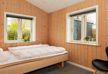 Soveværelse med træpanelvægge, to vinduer, en enkeltseng og minimalistisk indretning i Haderslev, Danmark.