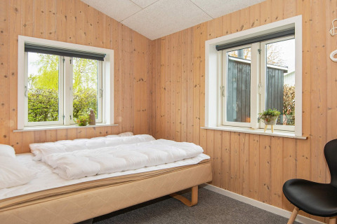 Chambre avec murs en bois, deux fenêtres, lit simple et décoration sobre dans un gîte à Haderslev, Danemark.