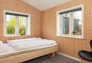 Chambre avec murs en bois, deux fenêtres, lit simple et décoration sobre dans un gîte à Haderslev, Danemark.