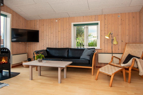 Wohnzimmer in einem Ferienhaus in Haderslev, Dänemark, mit Kamin, Holzverkleidung und Ledersofa.