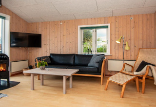 Wohnzimmer in einem Ferienhaus in Haderslev, Dänemark, mit Kamin, Holzverkleidung und Ledersofa.
