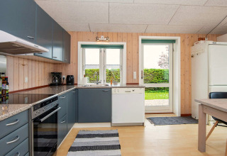 Cuisine moderne d’une maison de vacances à Haderslev, Danemark, avec armoires grises et vue sur le jardin.