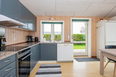 Cuisine moderne d’une maison de vacances à Haderslev, Danemark, avec armoires grises et vue sur le jardin.